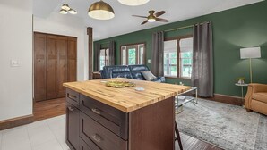 Een moderne keuken met een houten kookeiland, hanglampen, een plafondventilator en uitzicht op de buitenwereld door grote ramen.