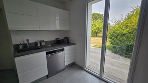 A modern kitchen with white cabinets, a black countertop, and a dishwasher. There is a sliding glass door leading to a wooden deck. - Luxury house near town and 150m from the ocean (Saint-Gildas-de-Rhuys)