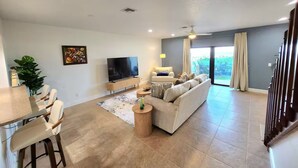 A modern living room with a sofa, TV, and dining area. - Sea Breeze Bungalow (Melbourne Beach)
