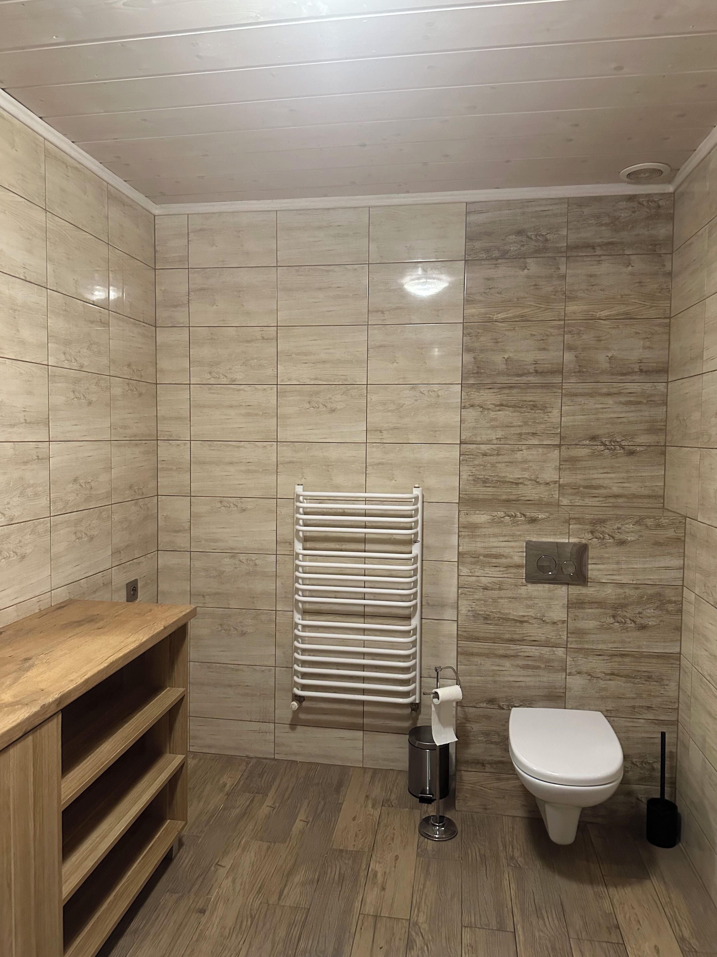 A modern bathroom with wooden flooring, a built-in toilet, a white toilet paper holder, and a towel rack.