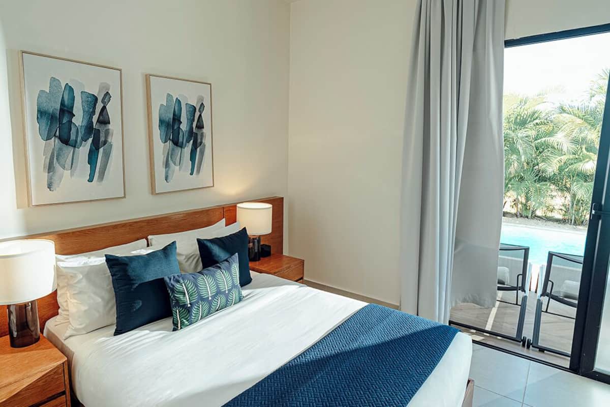 A hotel room with a large bed, two bedside tables, a nightstand, and a view of the pool through a glass door.