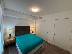 Un dormitorio con una cama, dos mesitas de noche, una lámpara de techo y dos puertas.