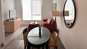 A modern living room with a round table, two chairs, a red sofa, a side table, a lamp, and a large mirror.