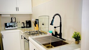 Une cuisine de taille réduite, avec des meubles blancs, une cuisinière à gaz, un évier et une petite plante en pot.