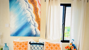 Une chambre à coucher avec un lit, des oreillers, un tableau, une fenêtre et un vase rempli de fleurs.