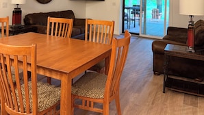 Een eethoek met een houten tafel en stoelen, een bank en een aan de muur bevestigde televisie.
