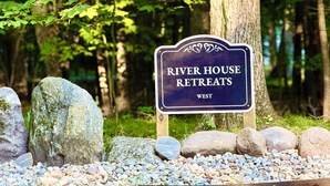 Naamplaatje voor River House Retreats West in een bebost gebied met grote rotsen en begroeiing.