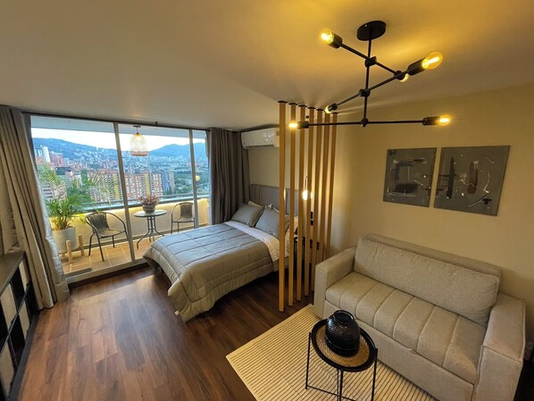 Une chambre d’hôtel moderne dotée d’un grand lit, d’un canapé, d’un balcon offrant une vue sur la ville et d’un luminaire au plafond au design unique.