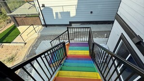 Eine Treppe mit einer regenbogenfarbenen Handlauf, die zu einem modernen Gebäude mit großen Fenstern und Blick auf eine grüne Rasenfläche führt.