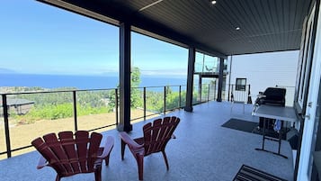 A spacious balcony with a clear view of the sea, furnished with wooden chairs and a grill.