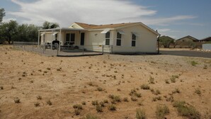 Einbungalow mit überdachter Terrasse, umgeben von vereinzelter Vegetation und wolkenlosem Himmel.