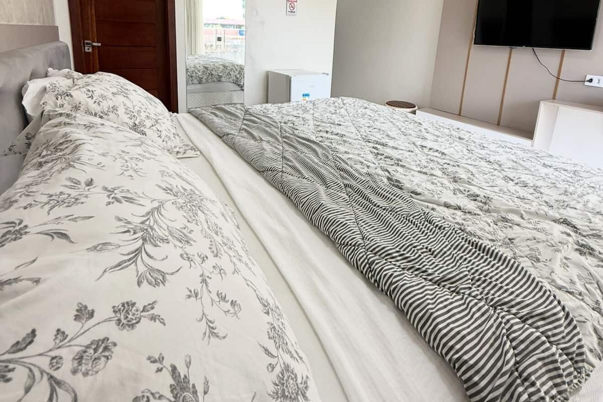 A hotel room with a large bed, a flat-screen TV mounted on the wall, and an air conditioning unit above the bed.