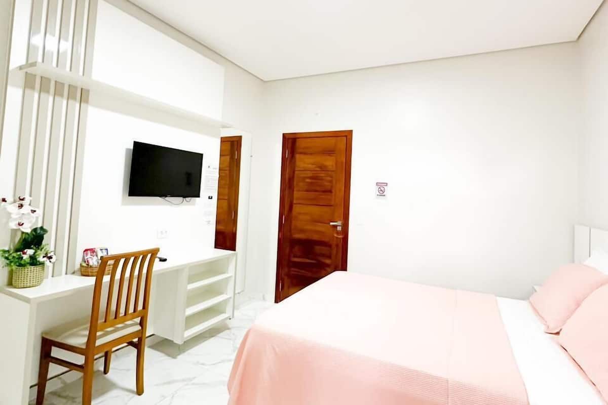 A bedroom with a bed, a desk, a chair, a TV, and a door.