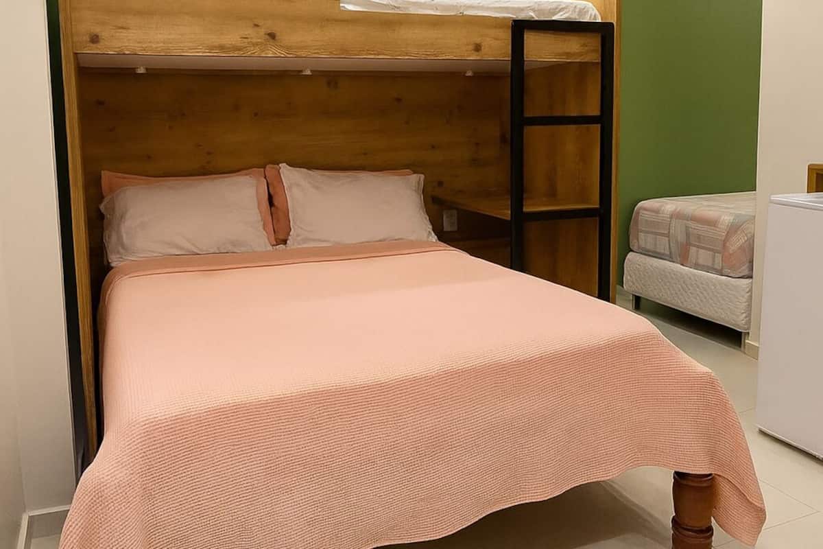 A bunk bed with a wooden headboard and a lower bed, both with white bedding. The room has green walls and a white floor.