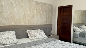A bedroom with a large bed, a headboard, and a wooden door.