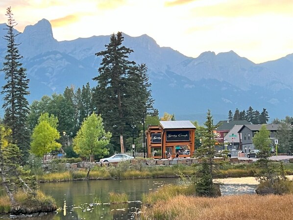 A lodge with a rustic wooden exterior, a pond in the foreground, and mountains in the background.
