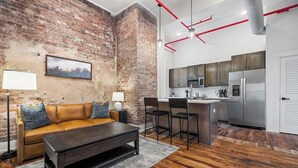 A modern living room with a brick wall, a sofa, a coffee table, and a kitchen area with a refrigerator and microwave.