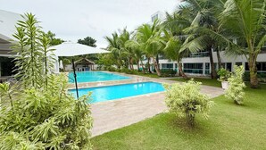 Ein Pool, umgeben von Palmen und Grünpflanzen, mit einem Gebäude im Hintergrund.