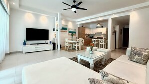Ein modernes Wohnzimmer mit Flachbildfernseher, weißen Sofas, einem Couchtisch und einem Deckenventilator.