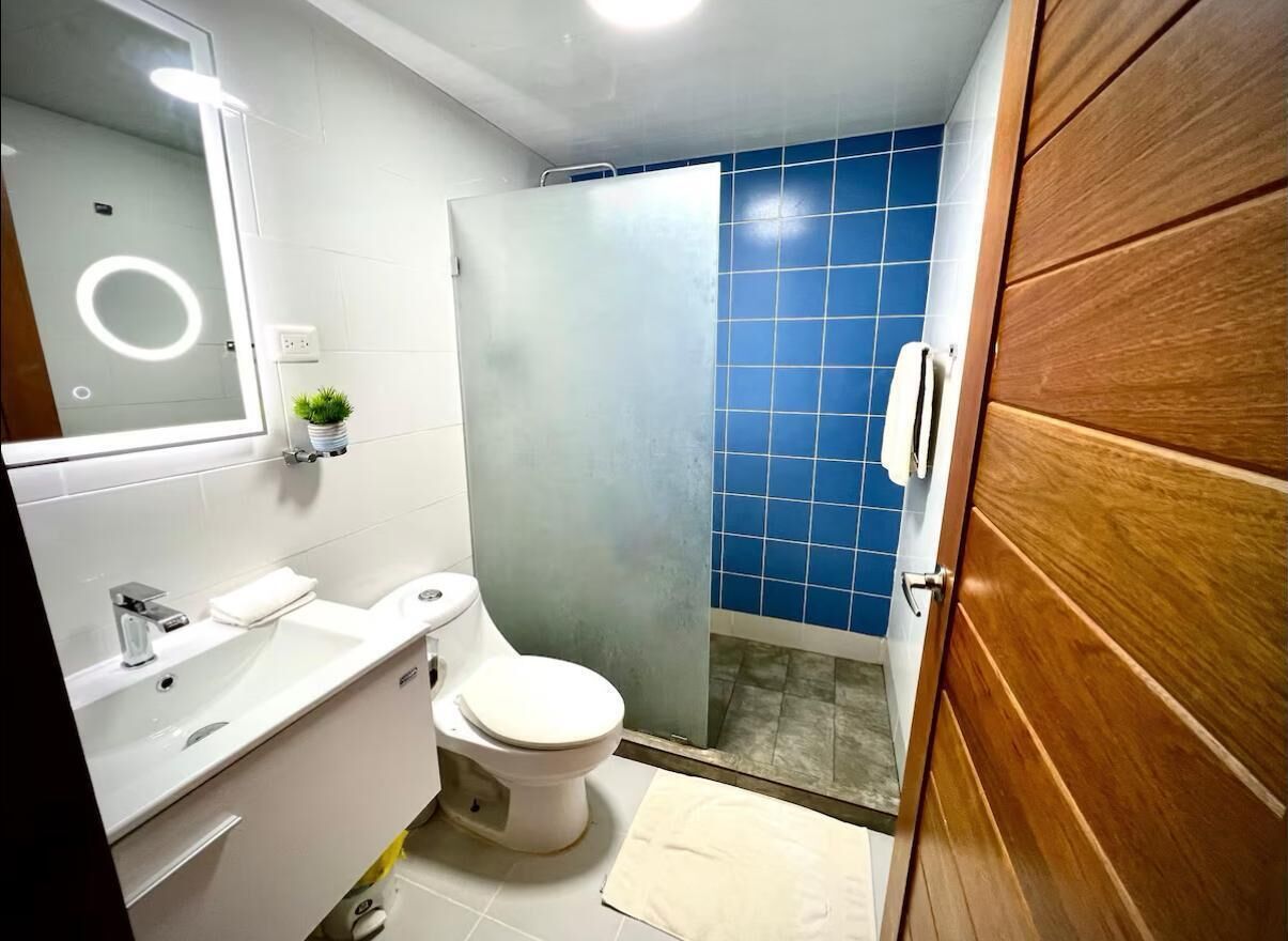 Casa de banho com lavatório branco, sanita e zona de duche revestida a azulejos azuis.