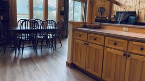 A wooden interior with a dining table and chairs, a kitchen counter, and large windows. - Creekside Chalet with private hot tub (Redmond)