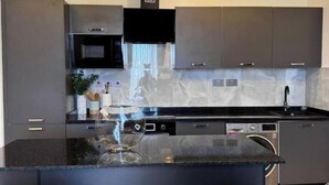 A modern kitchen with grey cabinets, a black countertop, and a built-in dishwasher.