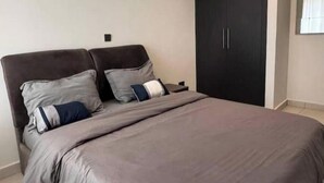 A bedroom with a bed, two nightstands, a dark wardrobe, and a window with curtains.