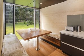 A modern kitchen with a wooden table, a built-in oven, and a view of a garden.