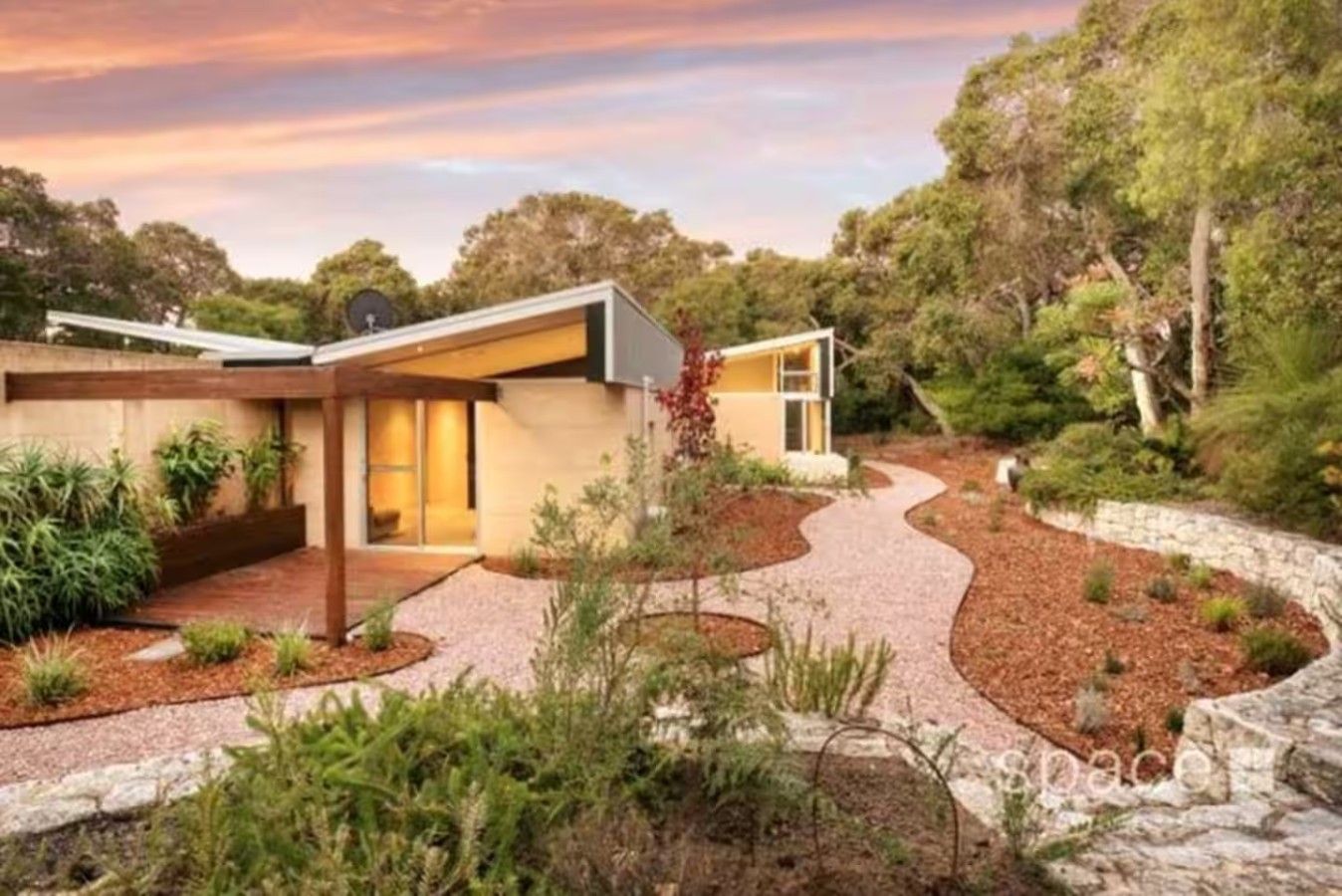 Une maison moderne avec une allée incurvée, entourée de jardins aménagés et d’arbres.