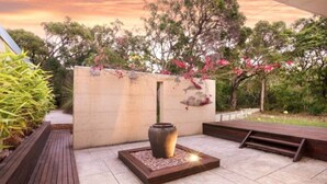 Un patio con un banco de madera, un jarrón decorativo y una pequeña chimenea.