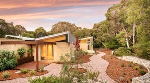 A modern house with a curved driveway, surrounded by landscaped gardens and trees.