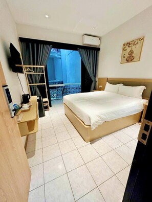 Ett hotellrum med en säng, ett skrivbord med en stol, en TV och en balkong med gardiner.