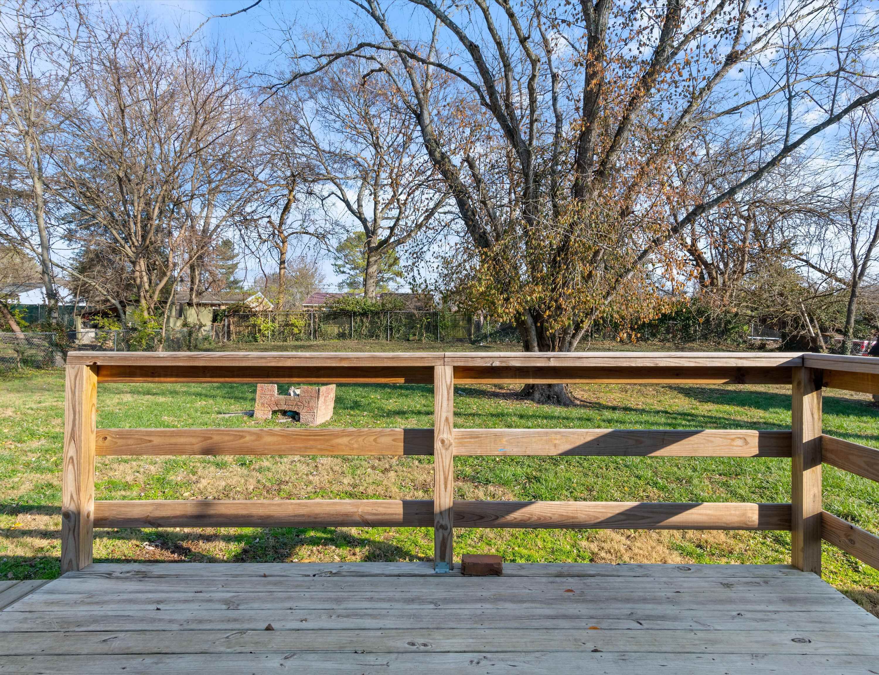 Une terrasse en bois avec une rambarde en métal, entourée de pelouse et d’arbres.