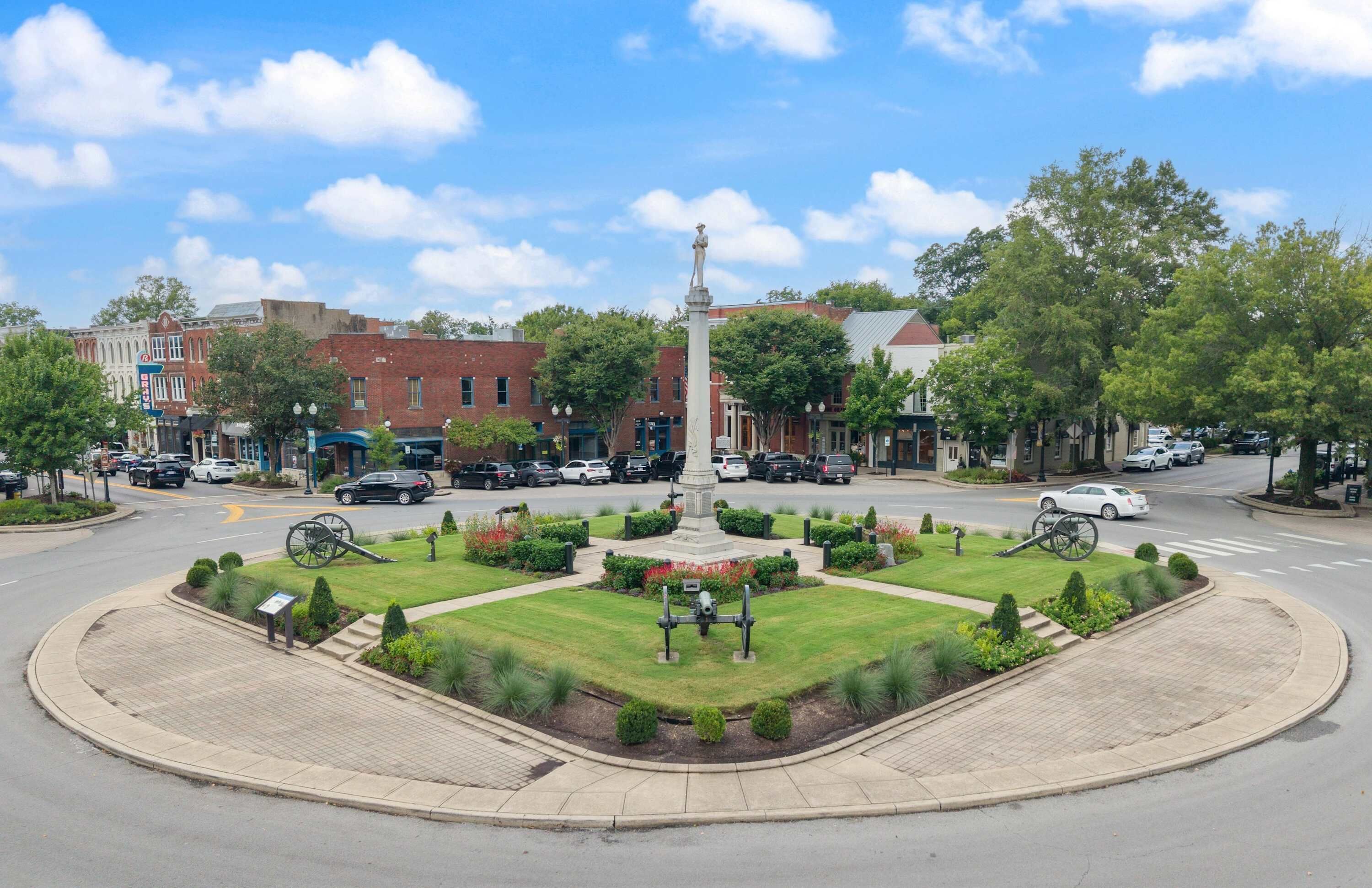 A central square with a monument, surrounded by a well-maintained lawn and a circular brick pathway.