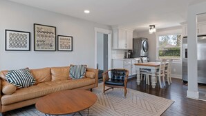 A modern living room with a leather sofa, a round coffee table, and a dining area with a wooden table and chairs. There is a kitchen in the background with white cabinets and stainless steel appliances. - Family Retreat - 1 Mile to The Factory at Franklin (Franklin)