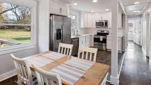 A modern kitchen with white cabinets, stainless steel appliances, and a dining area with a wooden table and white chairs. - Family Retreat - 1 Mile to The Factory at Franklin (Franklin)