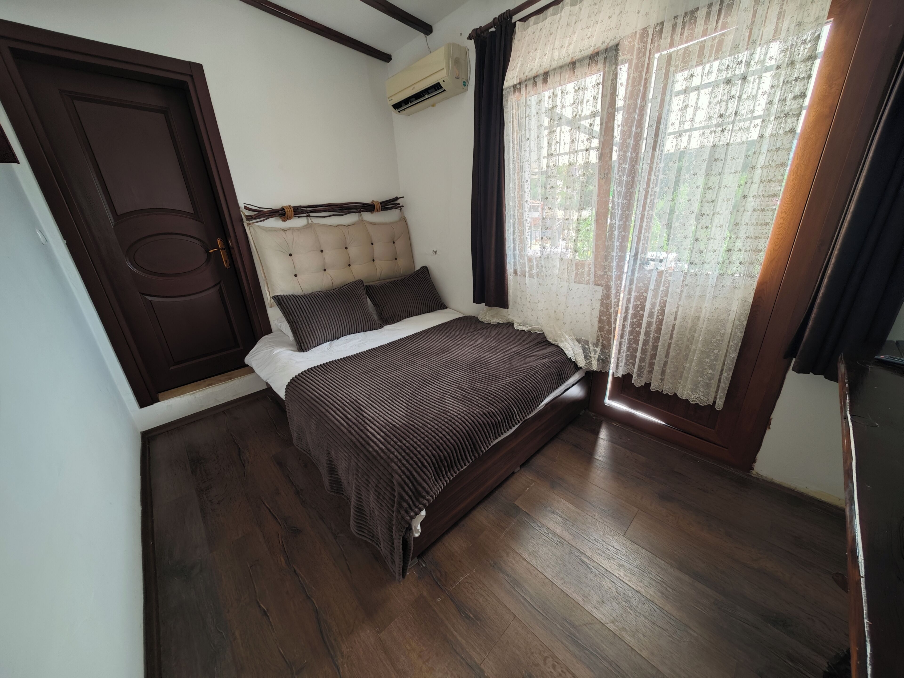 A bedroom with a bed, a door, an air conditioning unit, and a window with curtains.