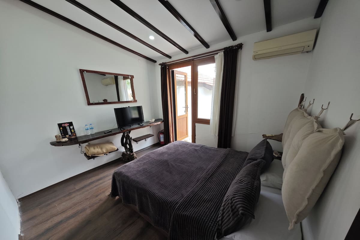 Une chambre à coucher avec un lit, une télévision, une étagère avec des objets, un miroir et une fenêtre.