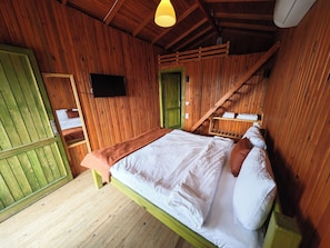 Una habitación de madera con una cama, un televisor y una puerta verde.