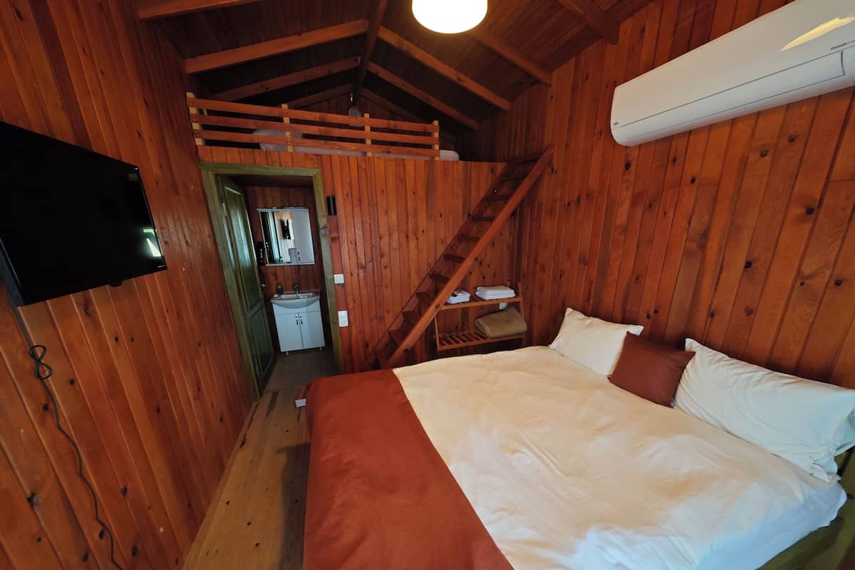 Una habitación de cabaña de madera con una cama, un televisor, un lavamanos y una escalera.