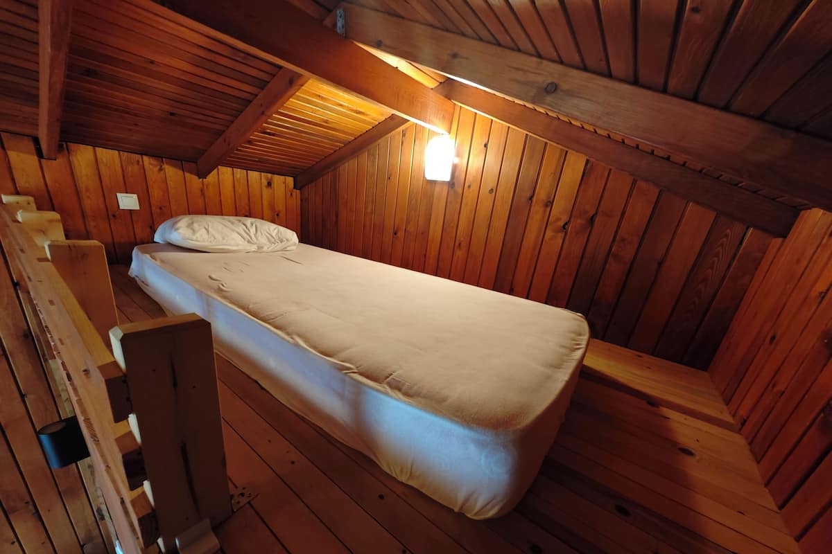 Una habitación de cabaña de madera con una cama individual, paredes de madera y techo inclinado.