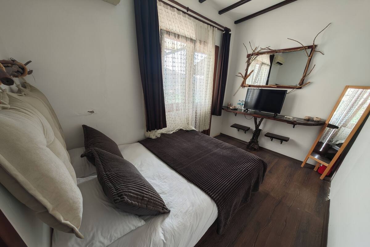 Un dormitorio con cama, televisión, espejo y ventana con cortinas.