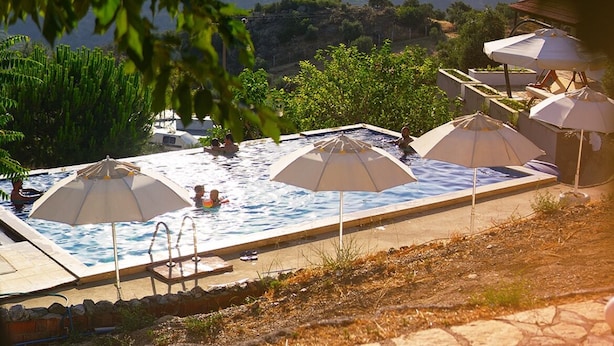 Una piscina infinita con sombrillas, un trampolín y vistas a montañas.