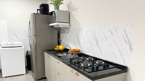Een compacte keuken met een gasfornuis, een spoelbak, een koelkast en een wasmachine.