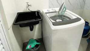 Een kleine badkamer met een wastafel, een wasmachine en een prullenbak.