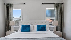 Ein Hotelzimmer mit einem großen Bett, zwei Nachttischlampen und Blick ins Freie durch zwei Fenster.