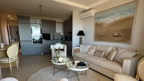 Un salon moderne avec un canapé beige, deux fauteuils, une table basse et un tableau représentant une scène de plage.