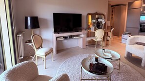Un salon moderne doté d’un téléviseur à écran plat, de sièges confortables, d’un coin repas et d’une cuisine en arrière-plan.