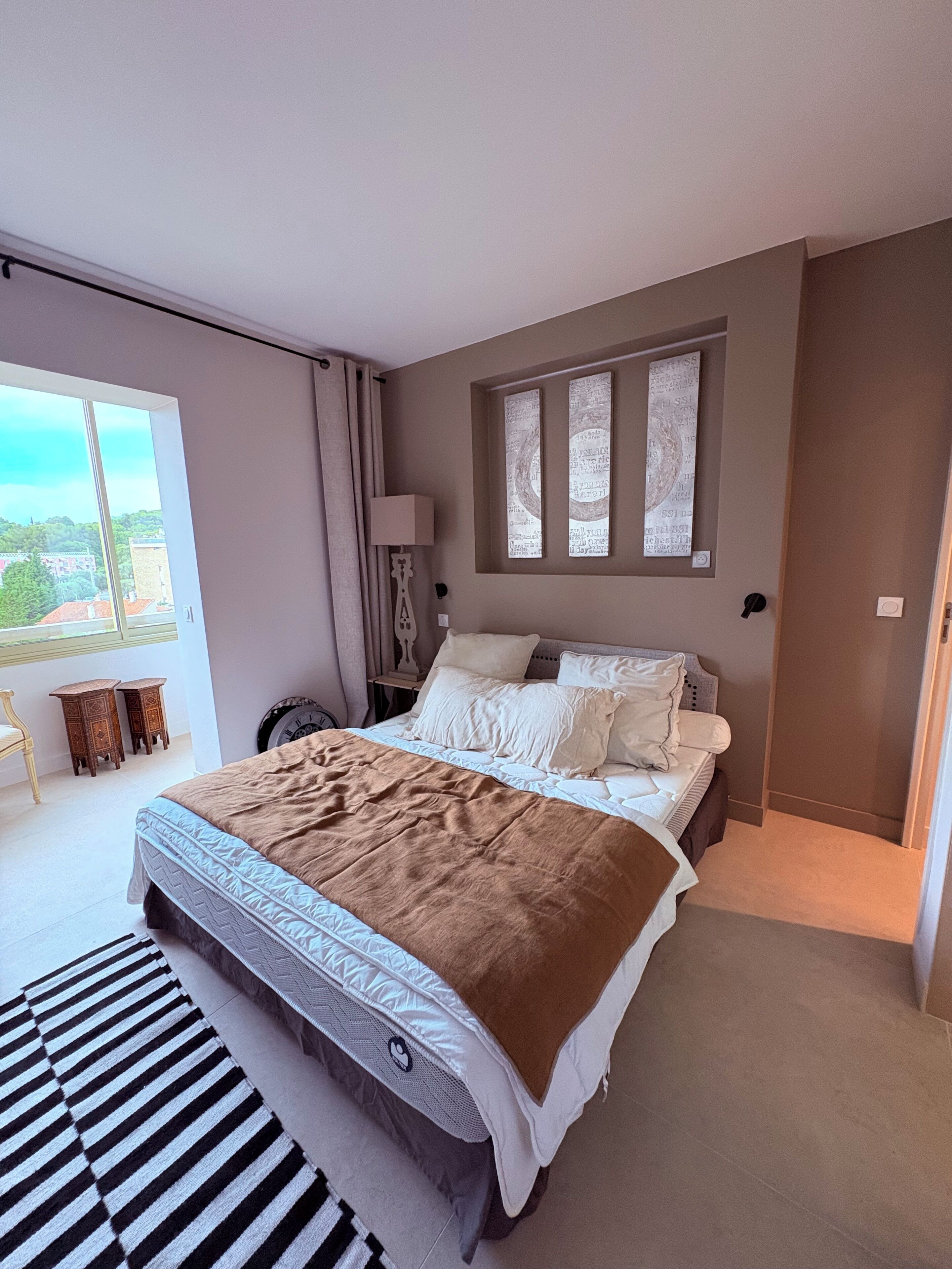 Un dormitorio con una cama grande, una ventana con cortinas, una lámpara y vistas al exterior.