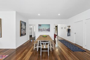 Un comedor moderno con una mesa y sillas de madera, un cuadro en la pared y un pasillo que conduce a otras habitaciones.